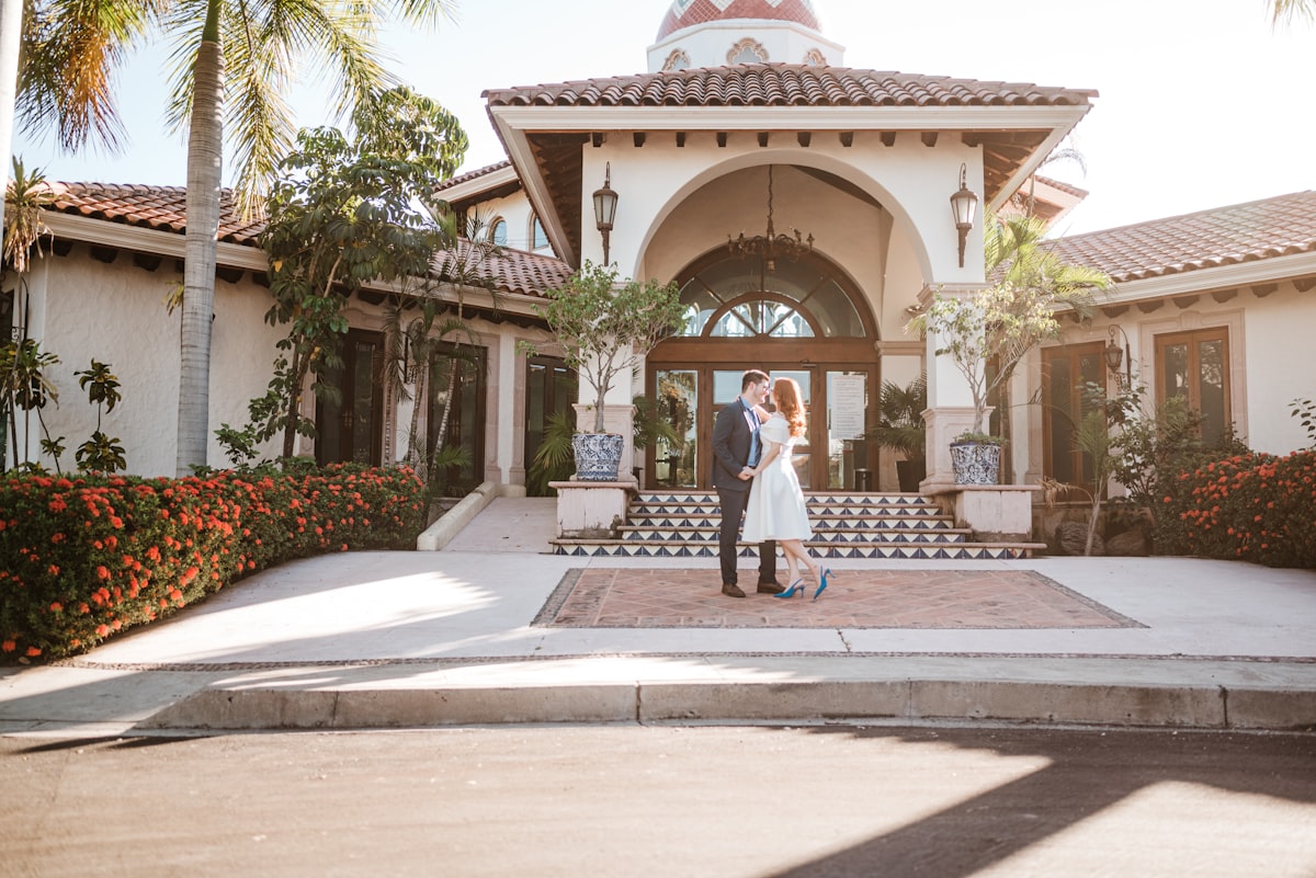 Romantic couple standing in front of Spanish-style architecture with warm lighting | Audaz Revista