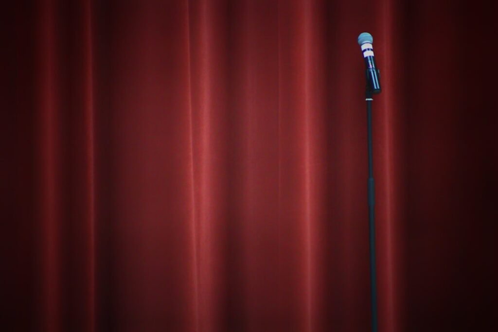 A stand-up comedy microphone on a stand under a spotlight on an empty stage