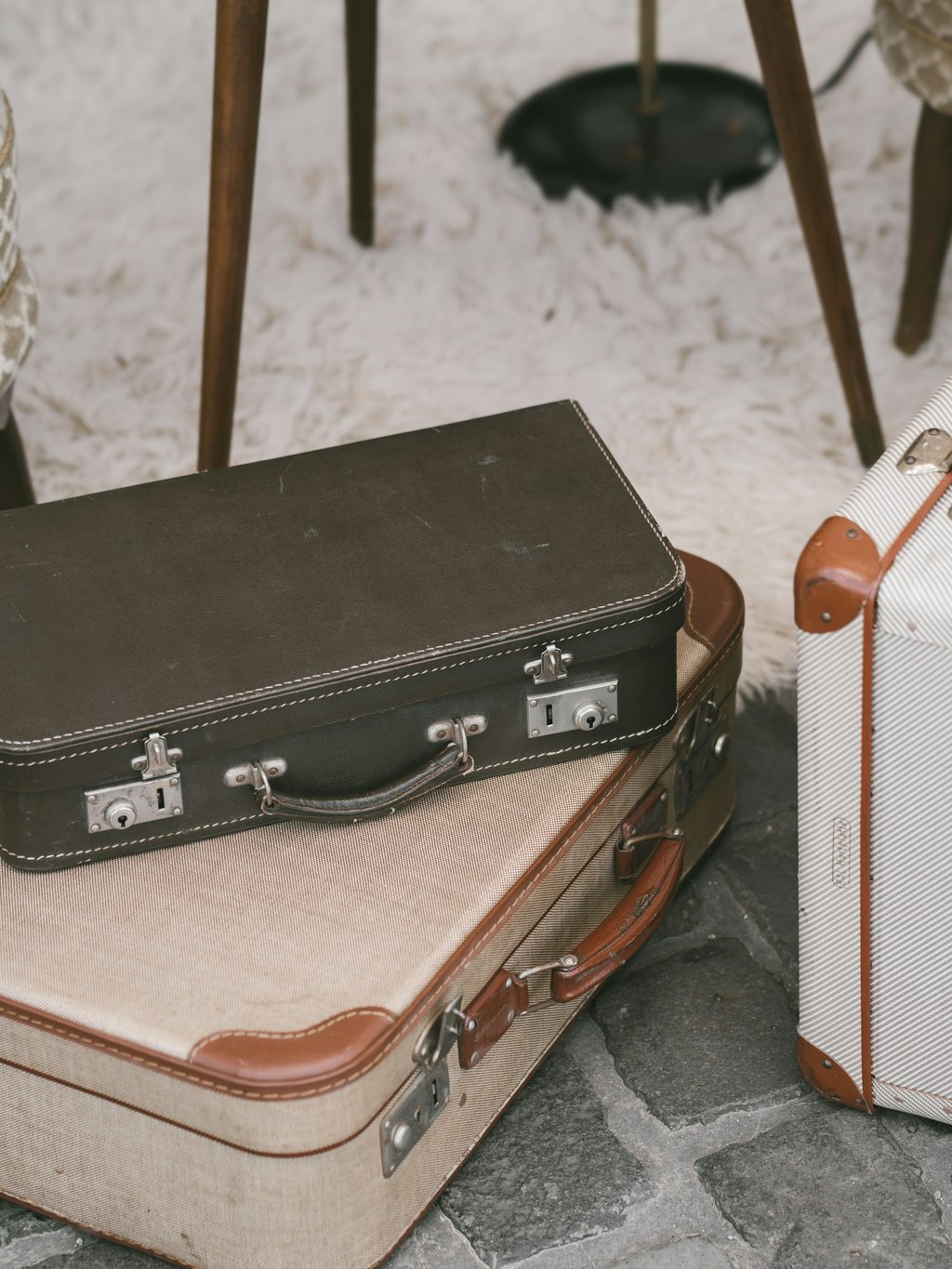 Vintage suitcases in dark brown, cream and tan leather stacked on a cobblestone floor beside a sheepskin rug