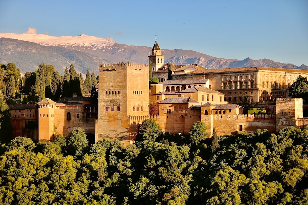 The Alhambra in Granada rising above the trees in late light, with the snow-capped Sierra Nevada behind it. The setting for a Spanish learner's guide to the city's accent, Arabic words and free tapas.