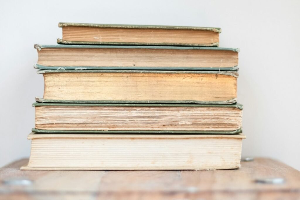 A stack of five old cloth-bound books with worn green covers on a wooden table against a white wall