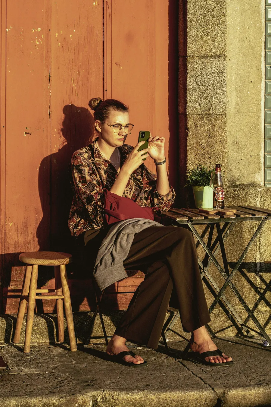 A woman sitting in a sunlit doorway, looking at her phone