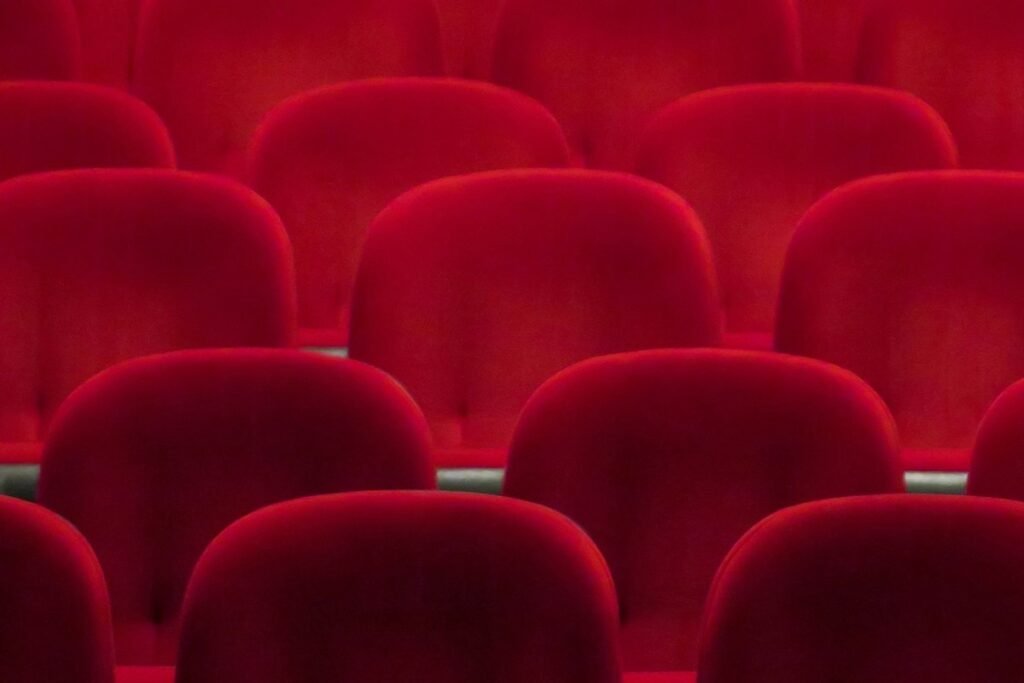 Rows of empty red velvet cinema seats seen from behind, filling the whole frame
